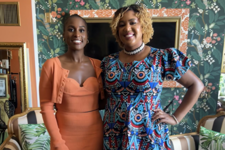 Issa Rae wears an orange long sleeved dress and Brooke Obie wears a colorful blue dress, they pose together